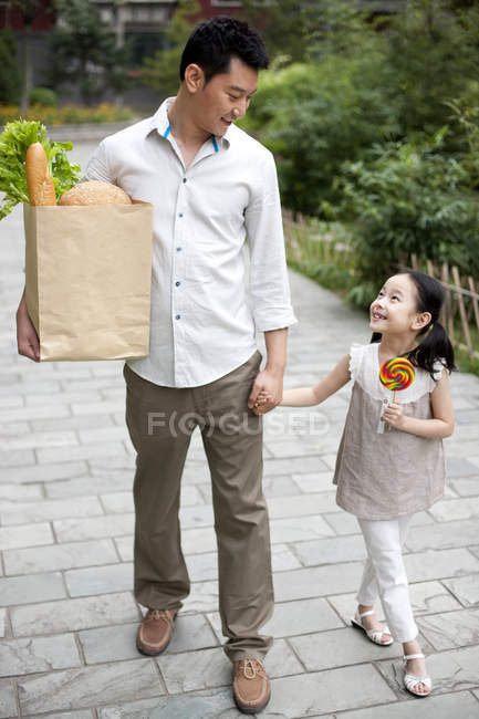 Padre e hija chinos caminando por la calle con comestibles - foto de stock