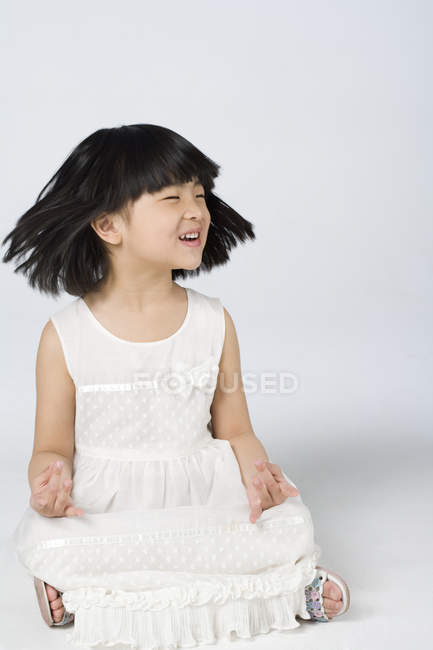 Kleines chinesisches Mädchen schüttelt den Kopf in Lotusposition auf grauem Hintergrund — Stockfoto
