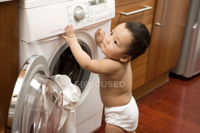 Bebé chino de pie y aferrado a la lavadora - foto de stock