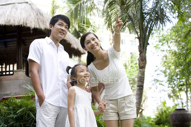 Padres chinos con hija de pie y señalando el complejo turístico - foto de stock