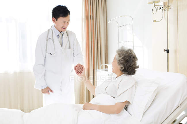 Chinese doctor holding hands with patient in hospital — Stock Photo