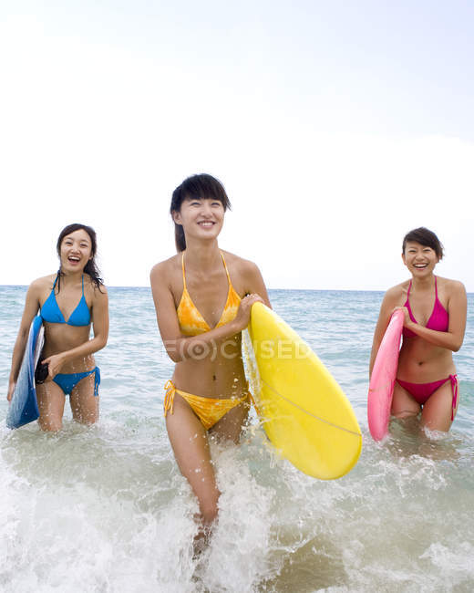 Jovens chinesas com pranchas de surf andando na água do mar — Fotografia de Stock