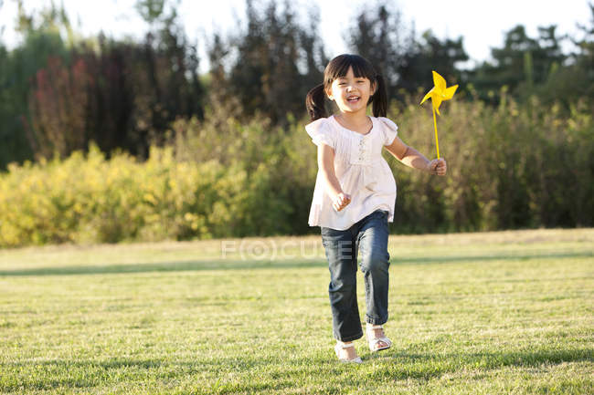 Pequena menina chinesa correndo no prado com pinwheel — Fotografia de Stock
