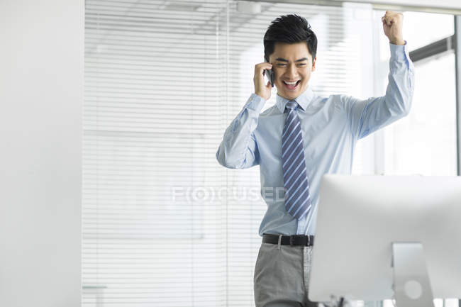 Cheerful Chinese businessman talking on phone in office — Stock Photo