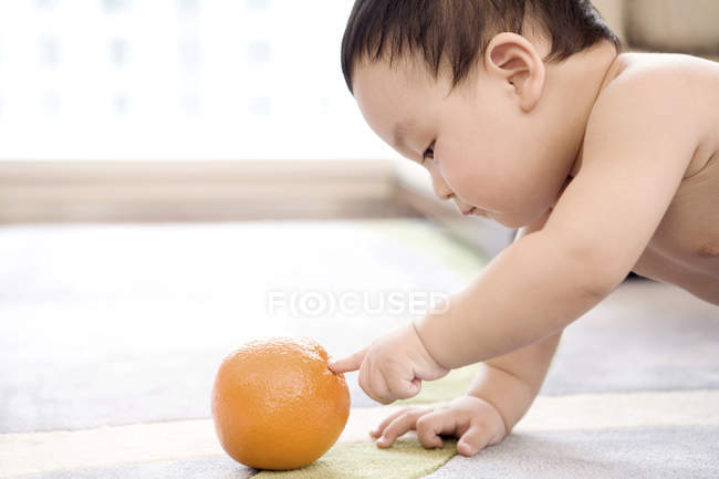 Китайский мальчик ползает и играет с апельсиновыми фруктами — стоковое фото