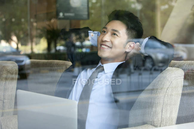 Chinese businessman sitting with hands behind head in cafe — Stock Photo