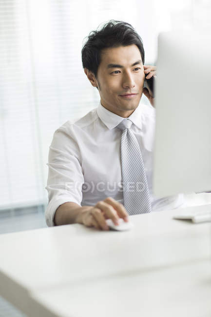 Китайский бизнесмен разговаривает по телефону за столом в офисе — стоковое фото