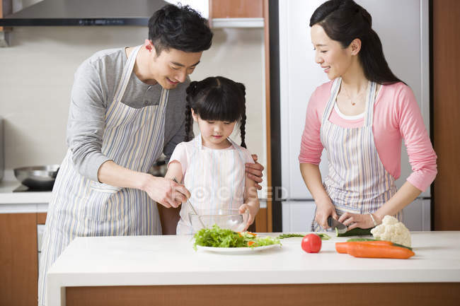 Famiglia cinese con figlia che cucina insalata in cucina — Foto stock