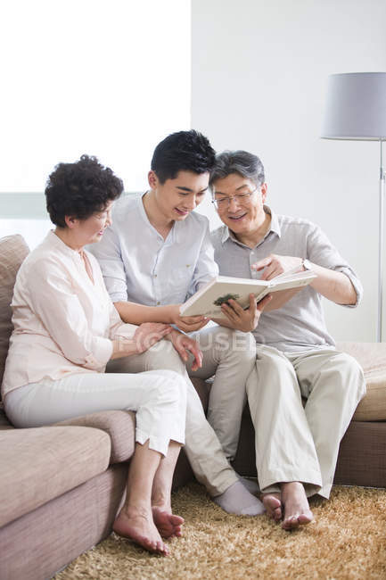 Chinese senior couple with adult son looking at photo album — Stock Photo