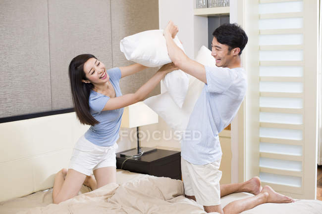 Young Chinese couple pillow fighting in bedroom — Stock Photo