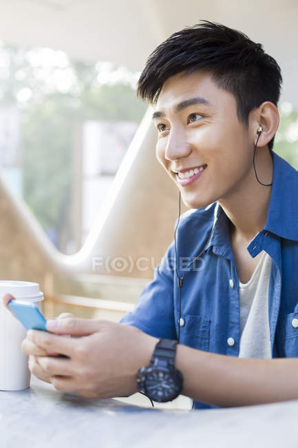 Chinese man listening to music with smartphone and holding coffee — Stock Photo