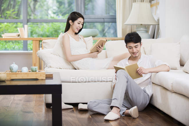 Joven pareja china leyendo libros en sala de estar - foto de stock