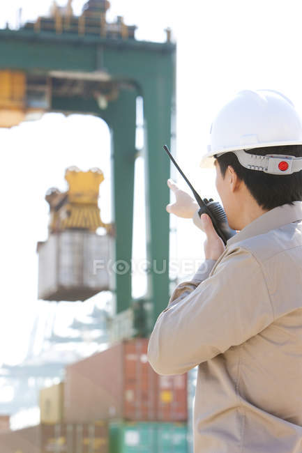 Shipping industry worker directing crane with walkie-talkie — Stock Photo
