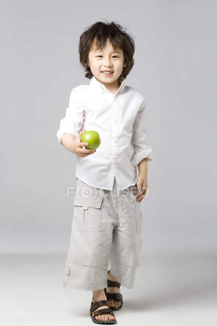 Asiático chico holding verde manzana en gris fondo - foto de stock
