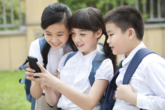 Chinese schoolchildren using smartphone in school yard — Stock Photo