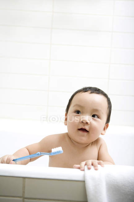 Chinese infant holding toothbrush in bathtub — Stock Photo