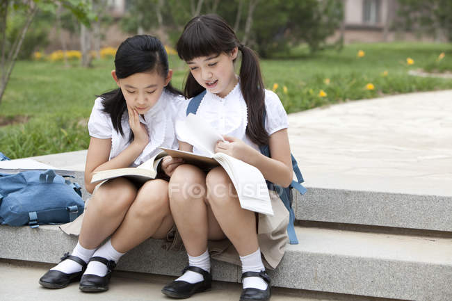 Schoolgirls sitting on steps and reading books — Stock Photo