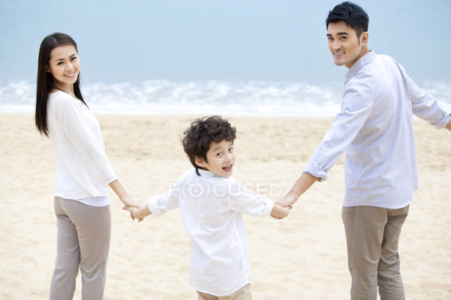 Famiglia cinese guardando indietro mano nella mano sulla spiaggia — Foto stock