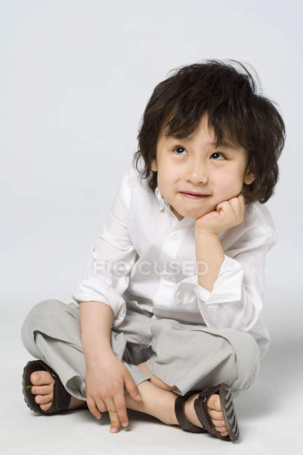Портрет маленького азиатского мальчика с рукой на подбородке на сером фоне — стоковое фото