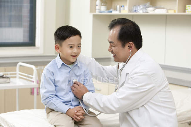 Chino maduro médico examinar chico en hospital - foto de stock