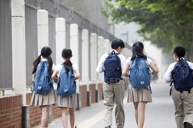 Вид сзади на школьников в школьной форме, идущих по тротуару — стоковое фото