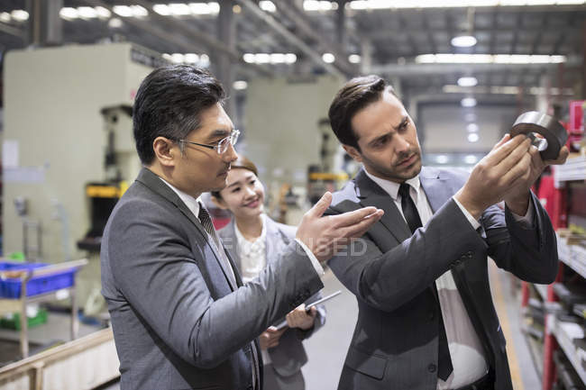 Business people checking machine parts in factory — Stock Photo