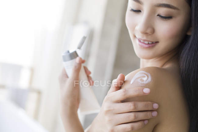 Chinese woman applying moisturizer to shoulder — Stock Photo