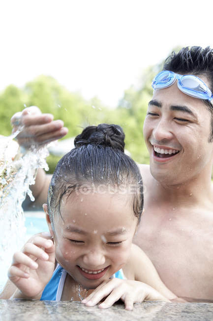 Padre e hija chinos jugando con agua en la piscina - foto de stock