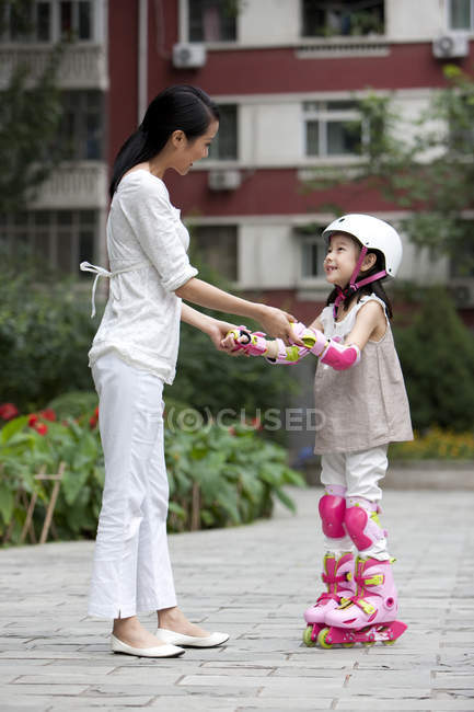Madre e hija chinas en patines tomados de la mano en la calle - foto de stock