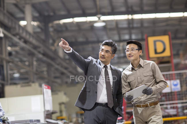Бизнесмен и инженер с помощью цифровых планшетов и разговоров на заводе — стоковое фото