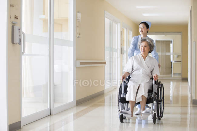 Enfermeira chinesa empurrando mulher sênior em cadeira de rodas — Fotografia de Stock
