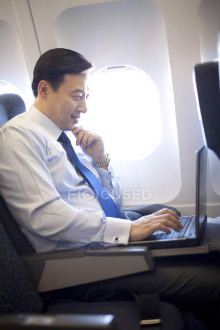 Uomo d'affari cinese che utilizza laptop in aereo — Foto stock