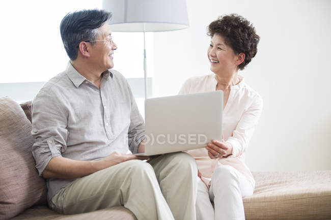Chinese couple using laptop and laughing on sofa — Stock Photo