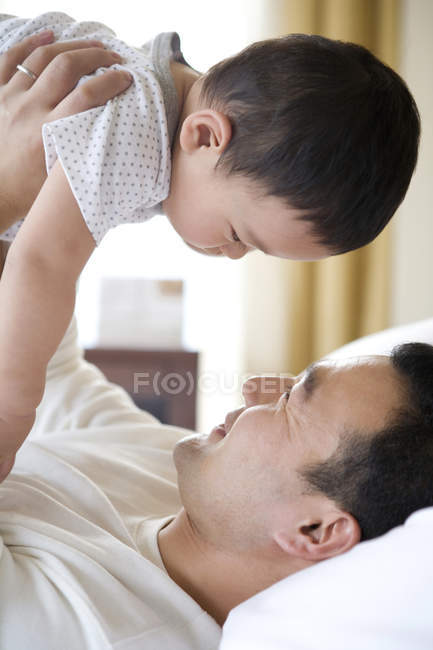 Chinese man holding aloft infant son on bed — Stock Photo