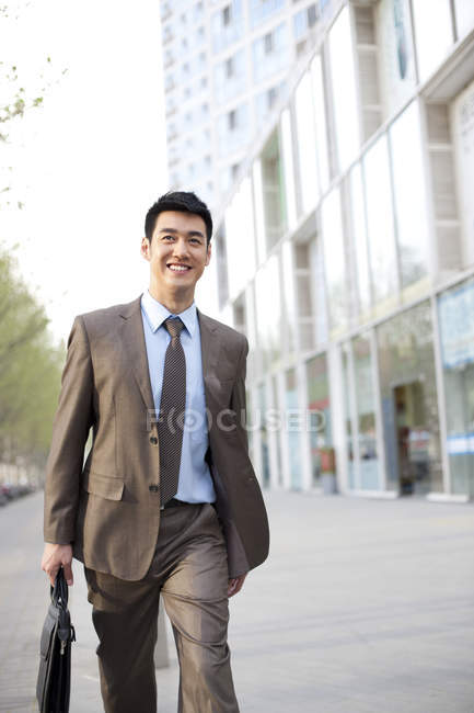 Confident Chinese businessman walking with briefcase in city downtown — Stock Photo