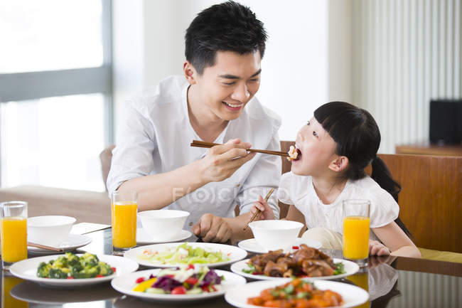 Chinese father feeding daughter with chopsticks at dinner table — Stock Photo