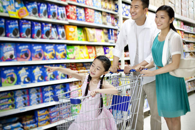 Padres chinos con hija en el carrito de compras en el supermercado - foto de stock
