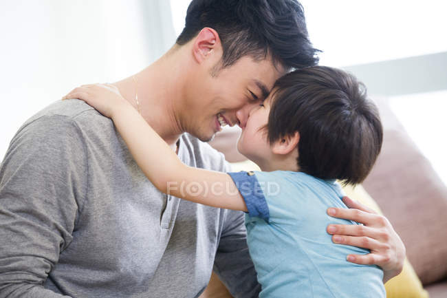 Cheerful Chinese father and son rubbing noses on sofa — Stock Photo