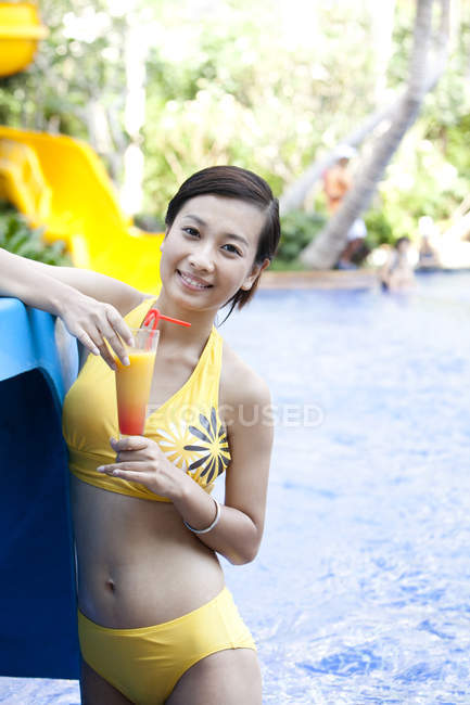 Chinese woman in bikini with cocktail at resort pool — Stock Photo