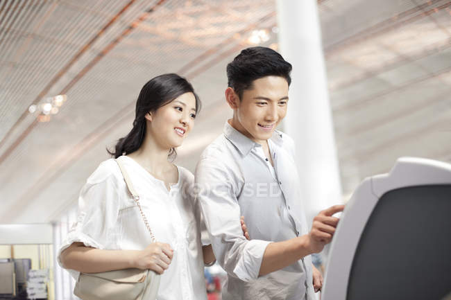 Chinese couple using ticket machine at airport — Stock Photo