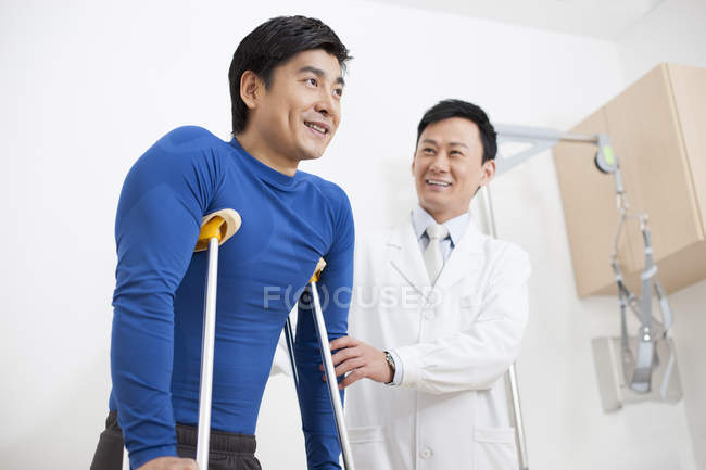 Chinese doctor helping patient with crutches — Stock Photo
