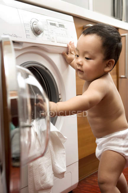 Bebê chinês colocando roupa na máquina de lavar roupa — Fotografia de Stock