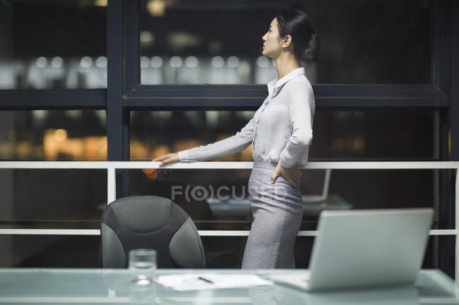 Chinese businesswoman looking through window in office — Stock Photo