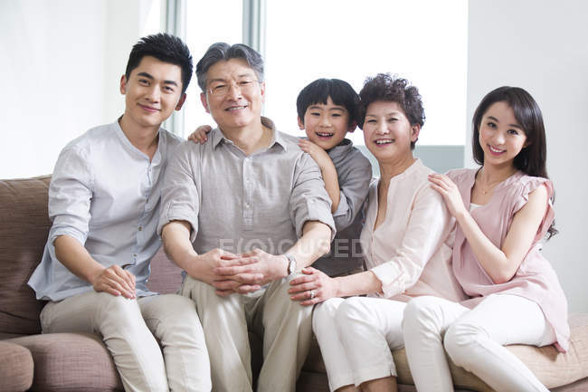 Retrato de la feliz familia china de tres generaciones sentadas en el sofá - foto de stock