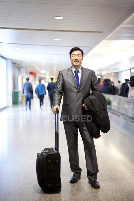 Hombre de negocios chino de pie con equipaje en el aeropuerto - foto de stock