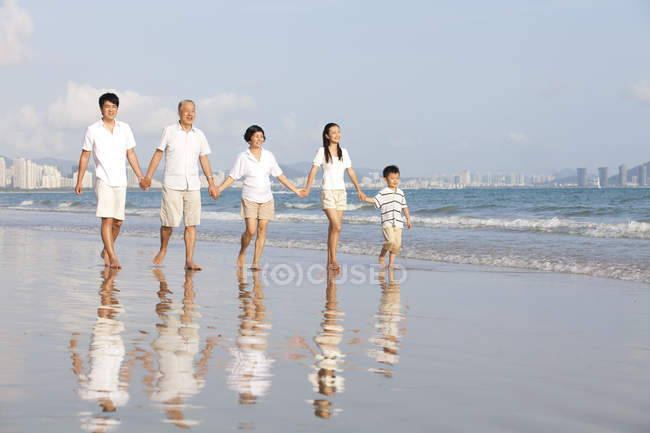 Familia china multi-generación caminando en la playa y tomados de la mano - foto de stock