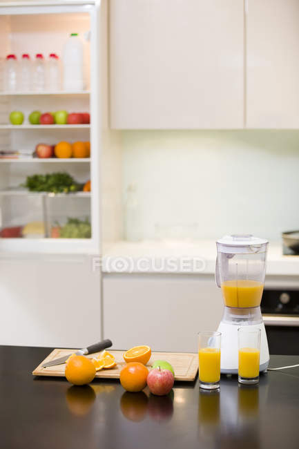 Frutas y zumo de naranja en exprimidor eléctrico en cocina casera - foto de stock