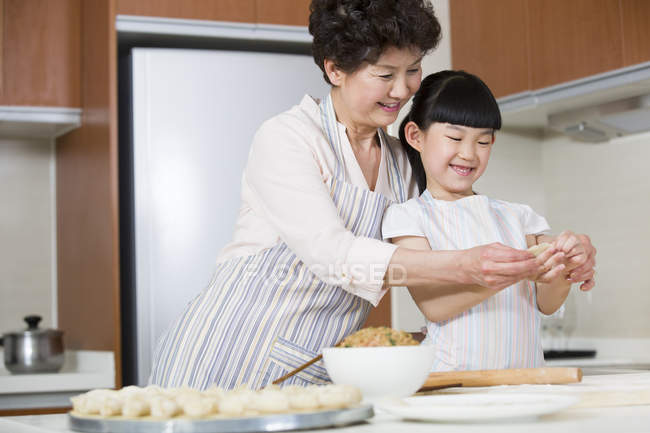Chinese grandmother and granddaughter making dumplings in kitchen — Stock Photo