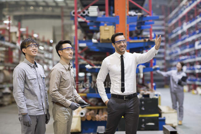 Businessman and Asian engineers talking at factory — Stock Photo