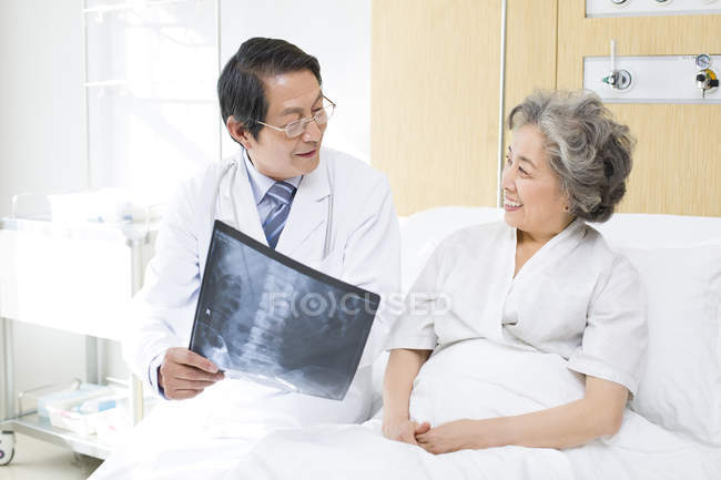 Médico chino mostrando imagen de rayos X al paciente - foto de stock